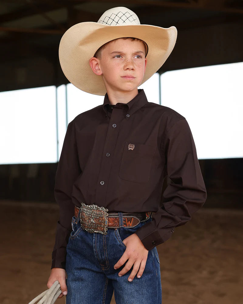 Young boy in cowboy attire with a wide-brimmed hat, brown shirt, and blue jeans.