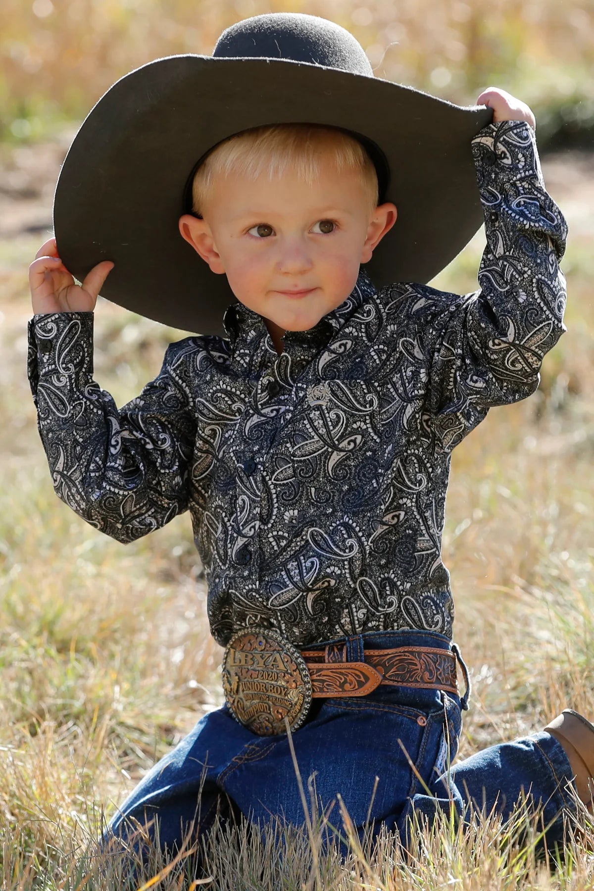 Cinch Toddler Paisley Print L/S Western Shirt. A child wearing a long sleeve black paisley button down shirt with a single patch pocket, paired with jeans and a wide-brimmed hat.
