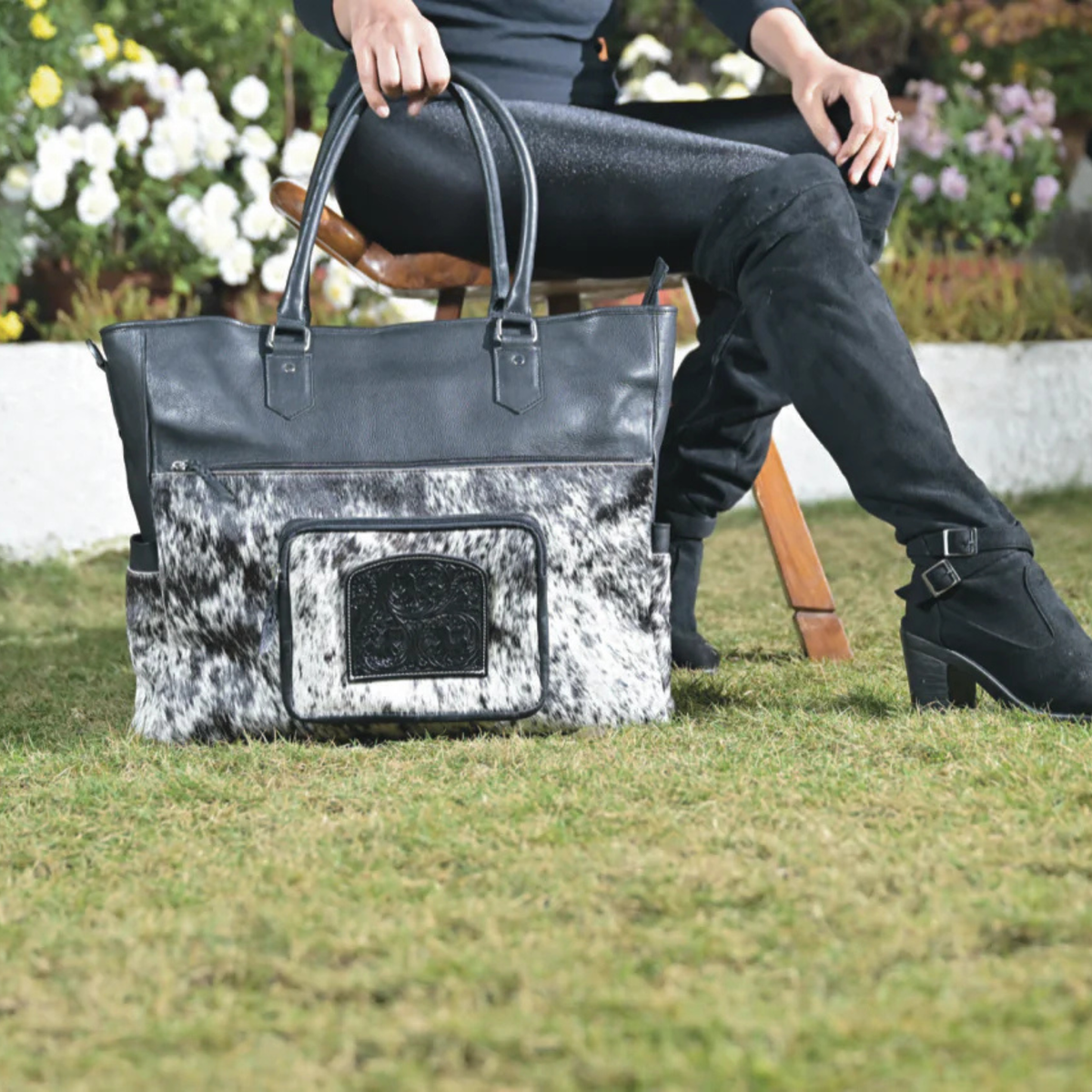 Cowhide &amp; Tooling Leather Nappy Bag. Person sitting on a bench with a large black and white patterned handbag in front of them.