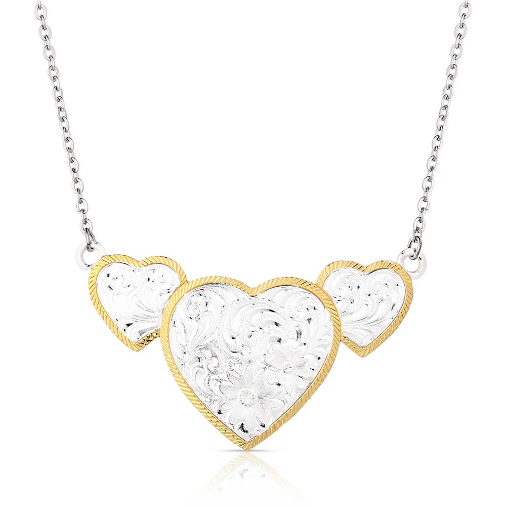 Montana Silversmiths Pure Heart Necklace. A necklace with three heart-shaped pendants, the largest in the center, with silver filigree and gold-tone roped borders on a silver chain.