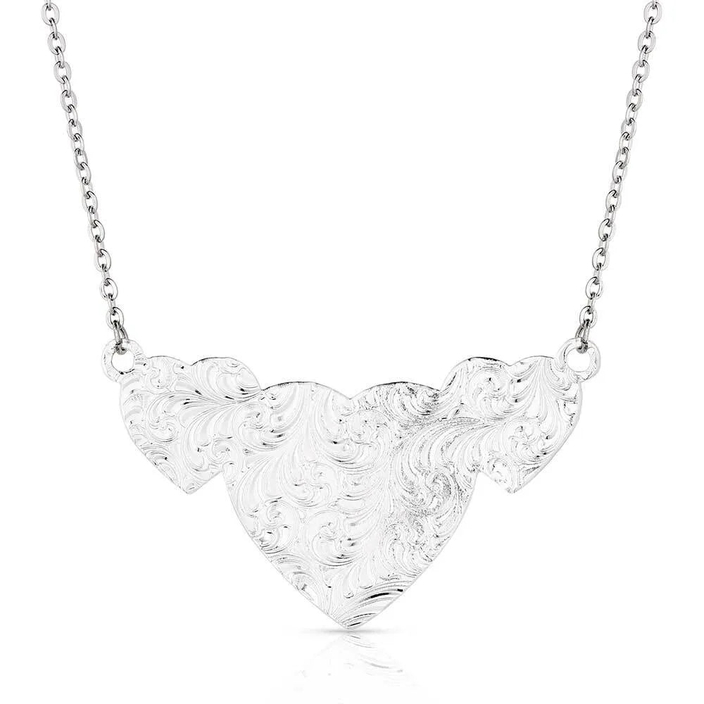 Montana Silversmiths Pure Heart Necklace. A necklace with three heart-shaped pendants, the largest in the center, with silver filigree and gold-tone roped borders on a silver chain.