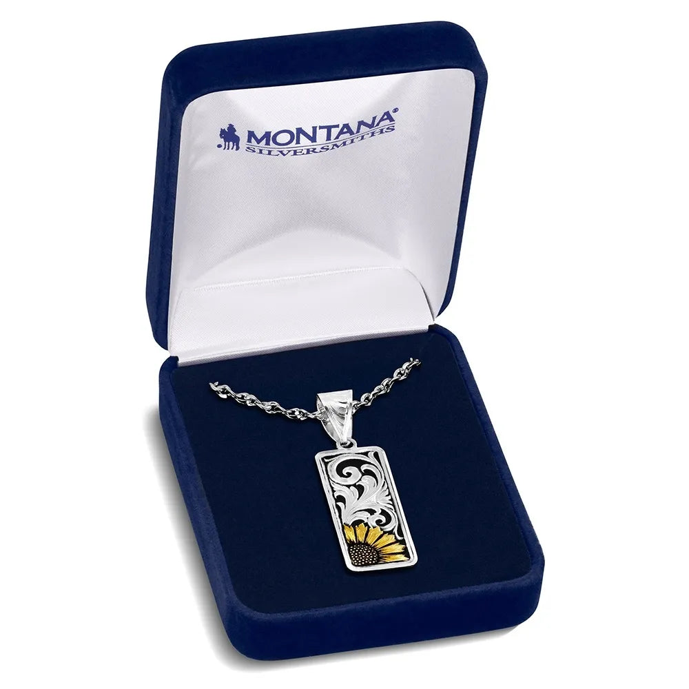 A Montana Silvermuts rectangular pendant necklace with a sunflower design, displayed inside an open navy blue velvet gift box with a white interior.