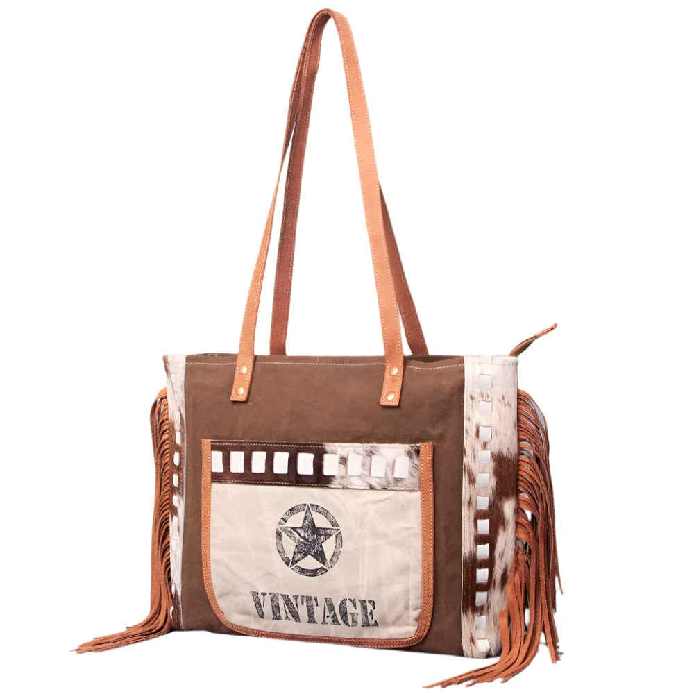 A brown and beige women's handbag with leather fringes and a 'Vintage' print on the front, featuring a star and the text 'American Darling'.