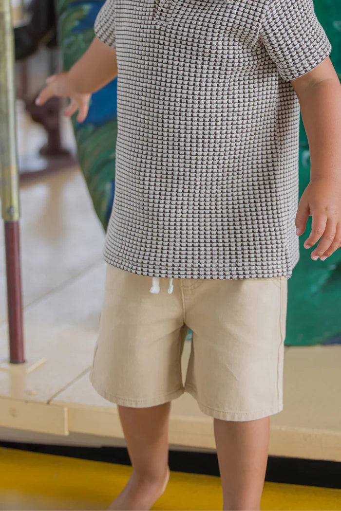 Milky Biscuit Short. Person wearing a patterned shirt and beige shorts in an indoor setting