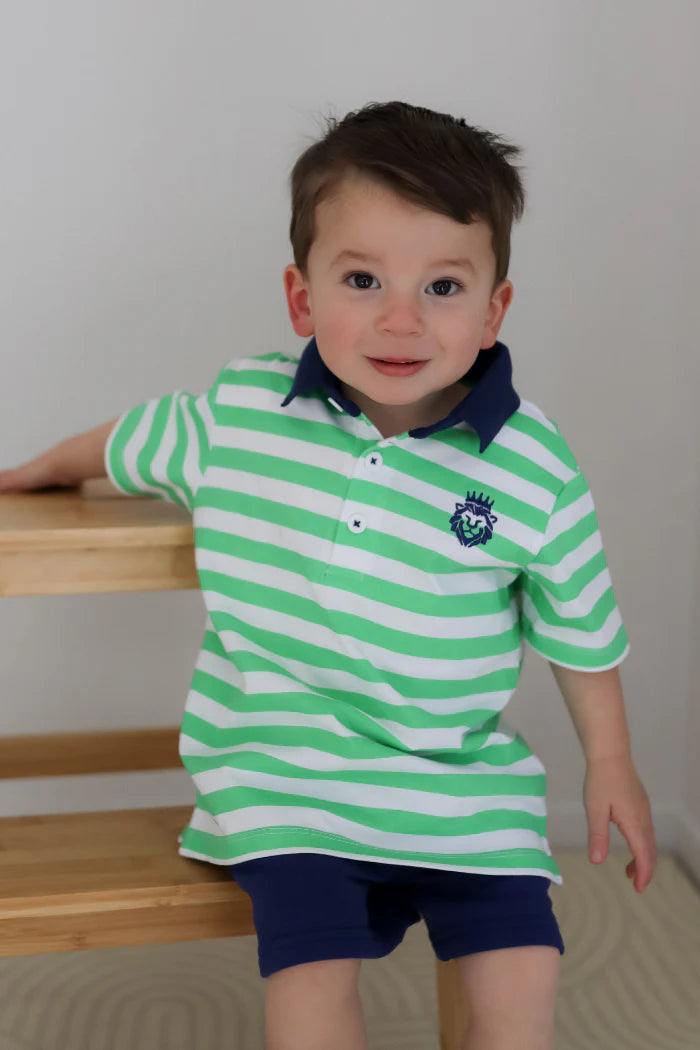 Milky Green Stripe Rugby. Child wearing a green and white striped polo shirt with a logo, standing indoors.