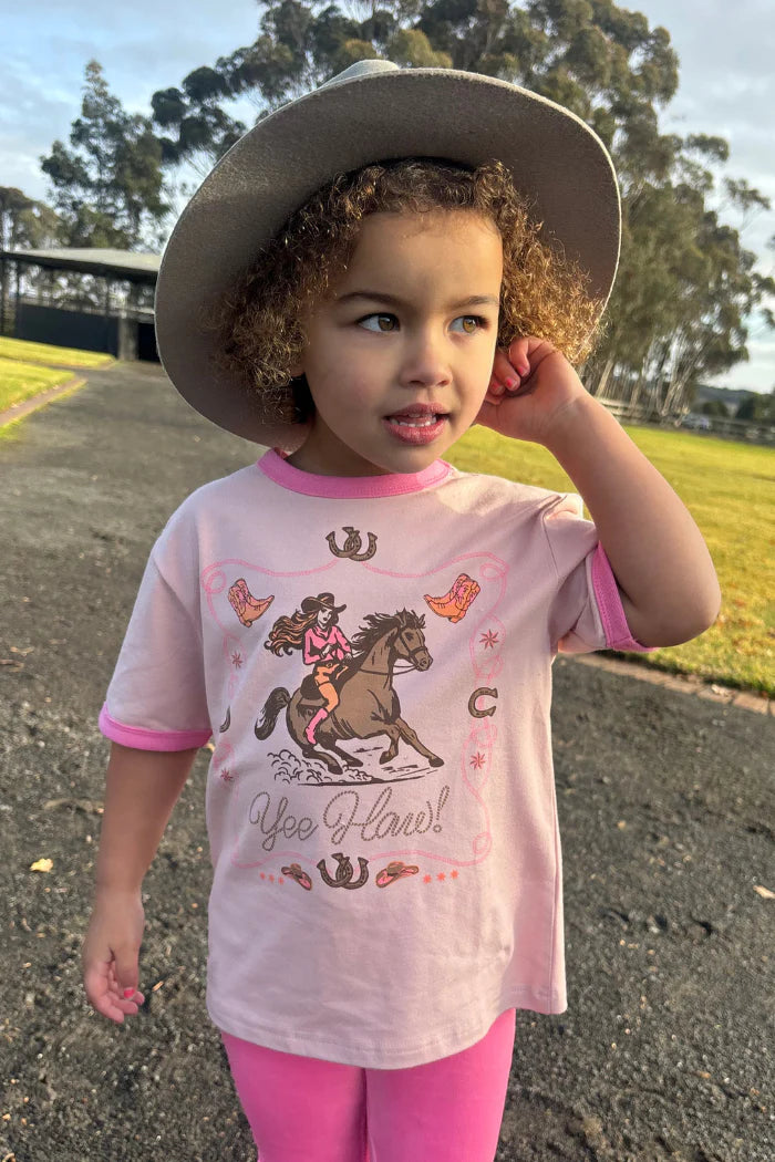 Milky Yee Haw Tee. Child wearing a pink shirt with a horse graphic and cowboy hat outdoors.