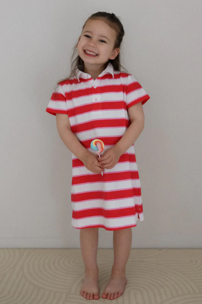 Milky Stripe Rugby Dress. Young girl wearing a red and white striped dress holding a lollipop against a plain background