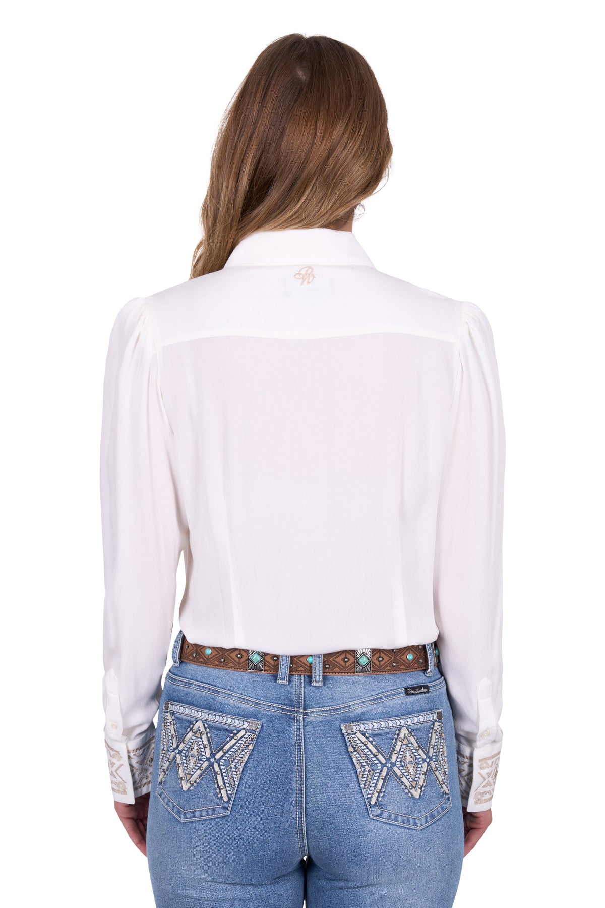 Pure Western Women's Monica L/S Western Shirt. Woman wearing a white blouse and blue jeans with intricate designs on a white background
