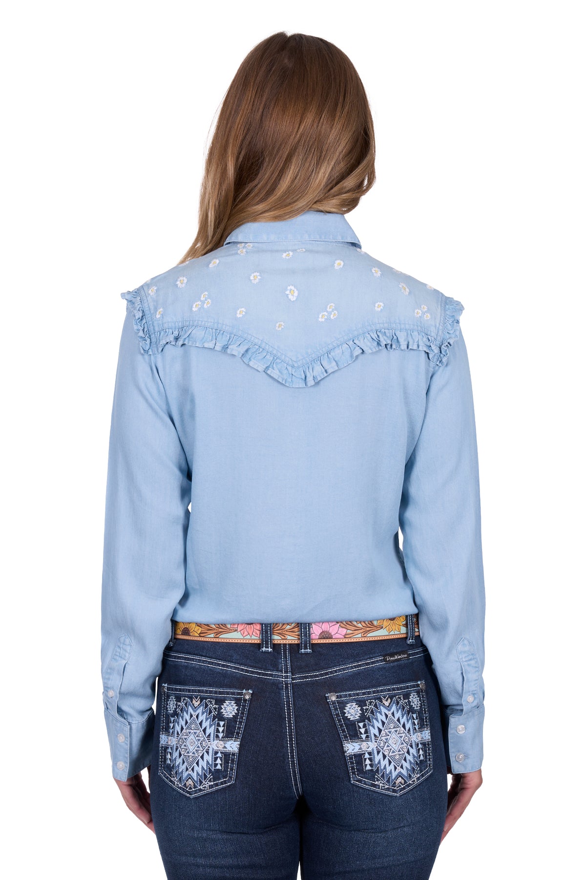 Pure Western Women's Phoebe L/S Western Shirt. Woman wearing a light blue denim shirt with floral embroidery and dark blue jeans on a white background