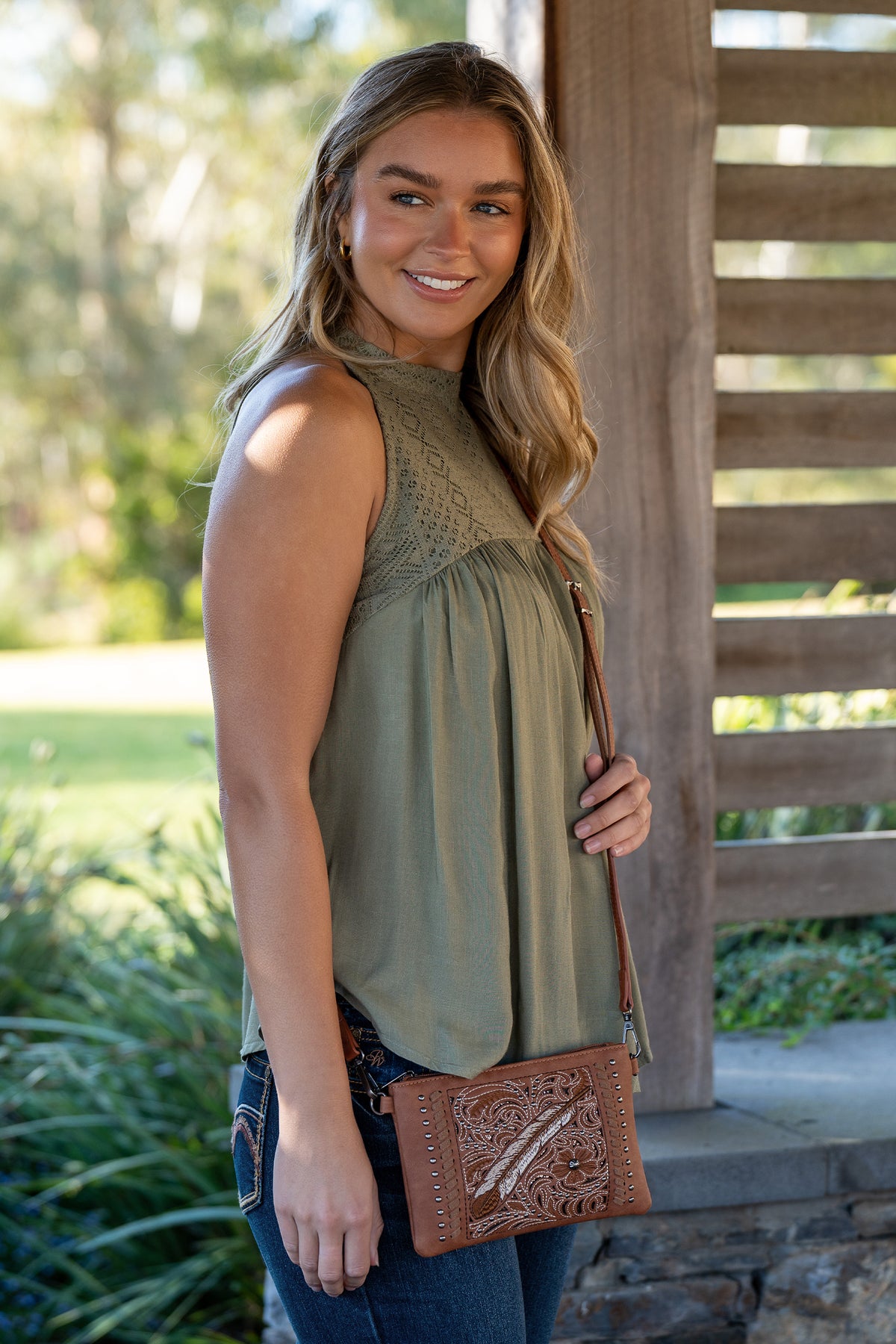 Pure Western Drew Western Bag. Woman holding a brown leather bag outdoors with greenery in the background