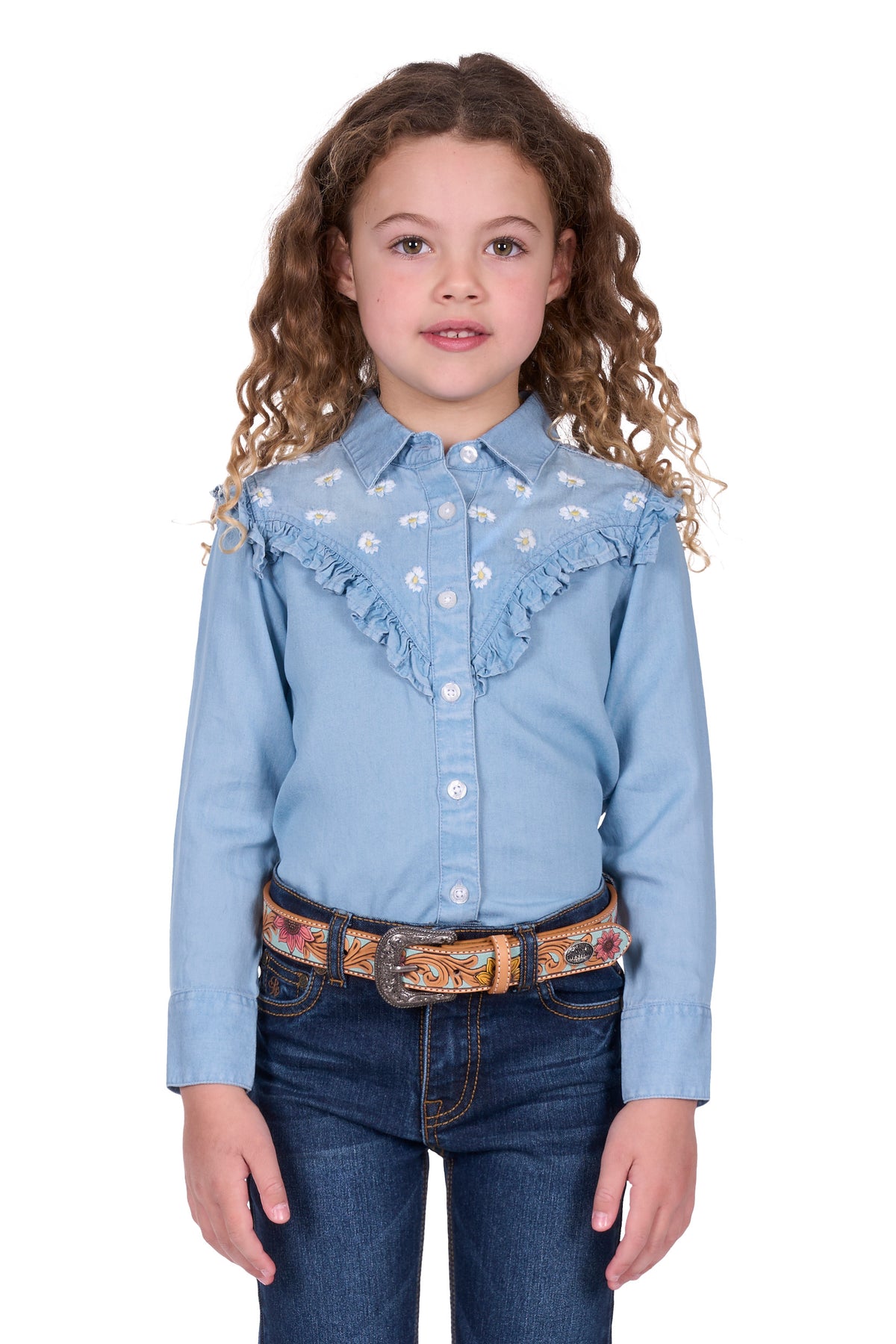 Pure Western Girl's Pheobe L/S Western Shirt. Young girl wearing a light blue denim shirt with ruffles and dark blue jeans on a white background