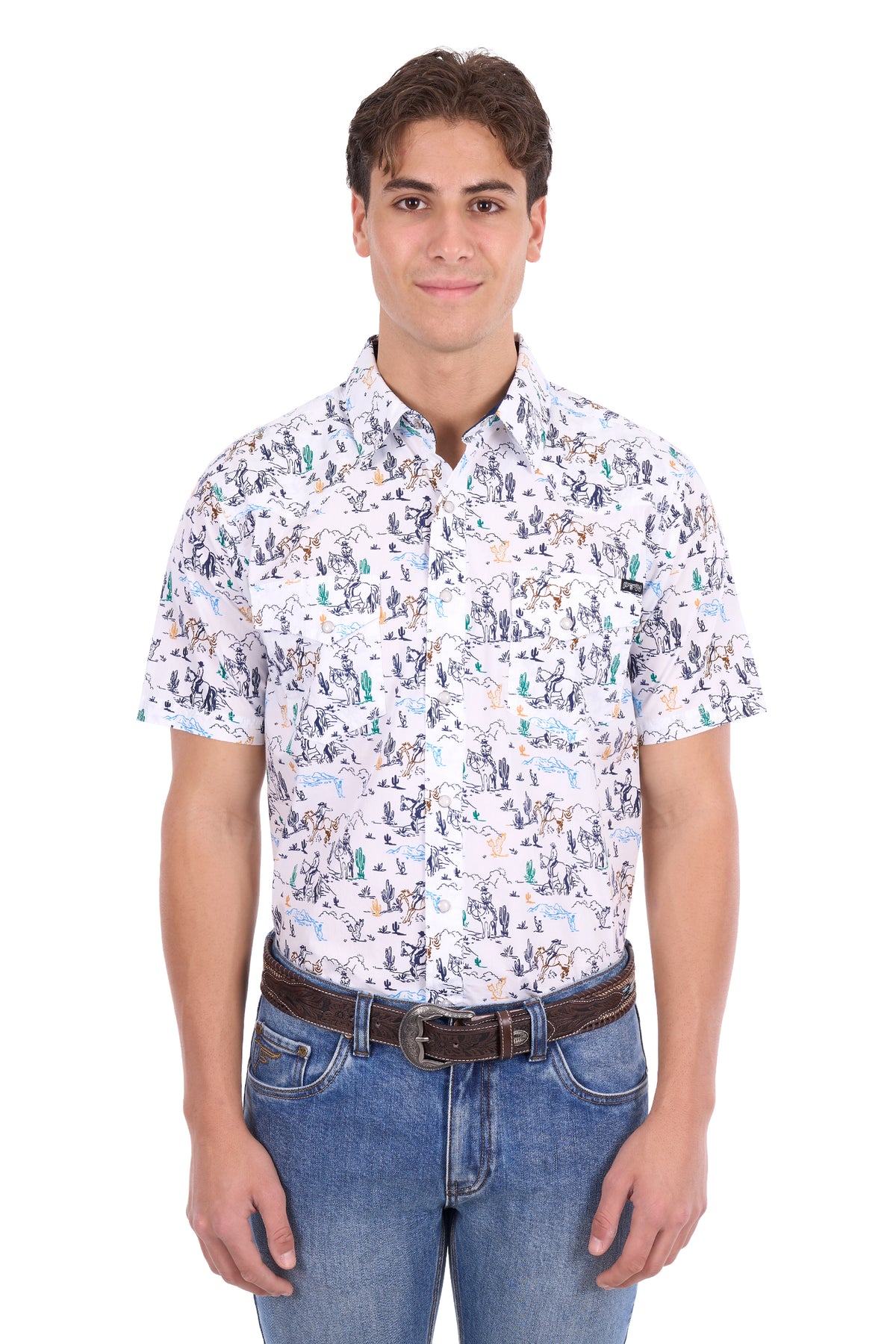 A man wearing a short-sleeve button-up shirt with a dense multicolor print of figures and objects on a white background, paired with blue jeans and a brown belt, against a plain white studio background.