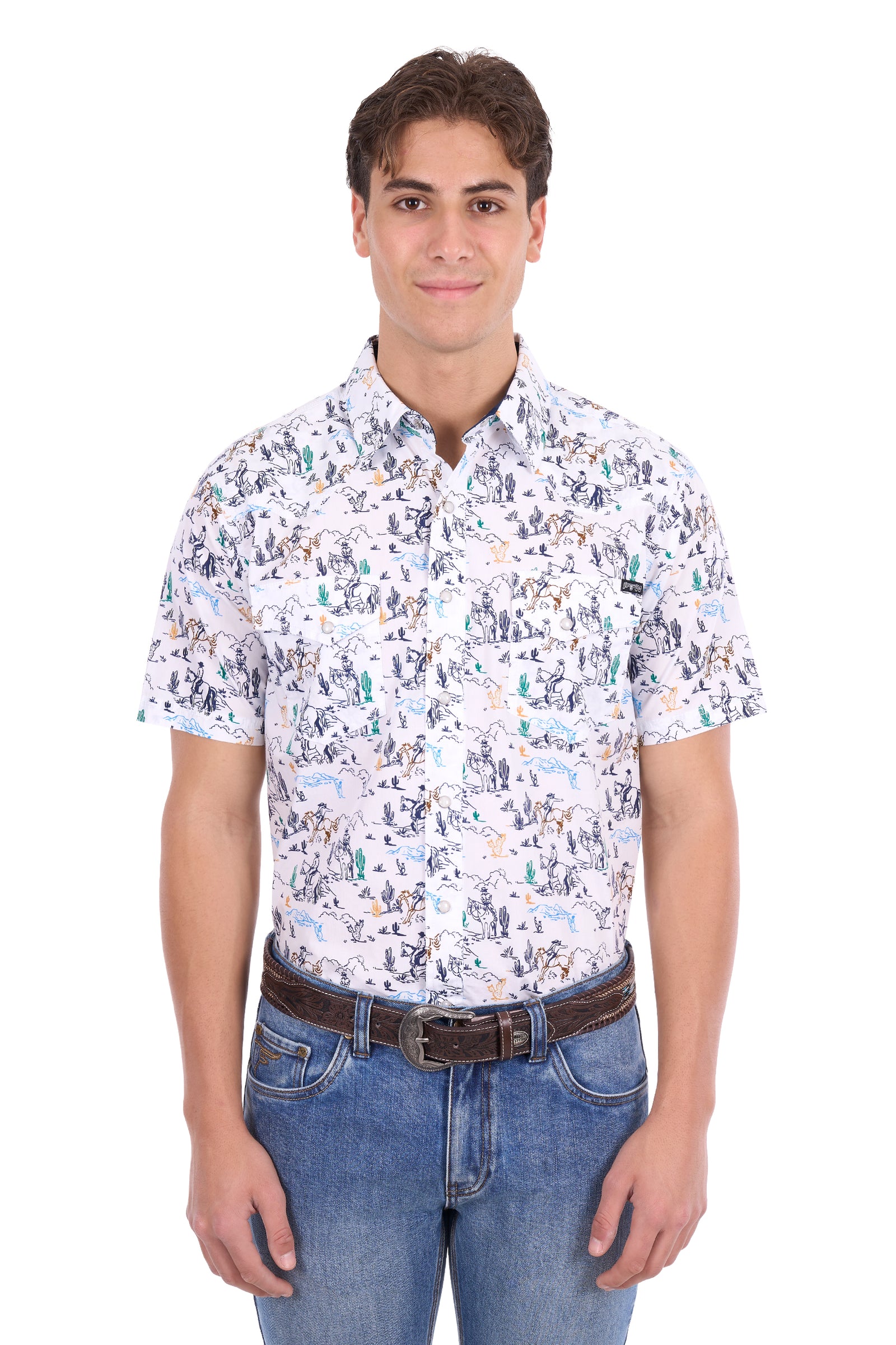 A man wearing a short-sleeve button-up shirt with a dense multicolor print of figures and objects on a white background, paired with blue jeans and a brown belt, against a plain white studio background.