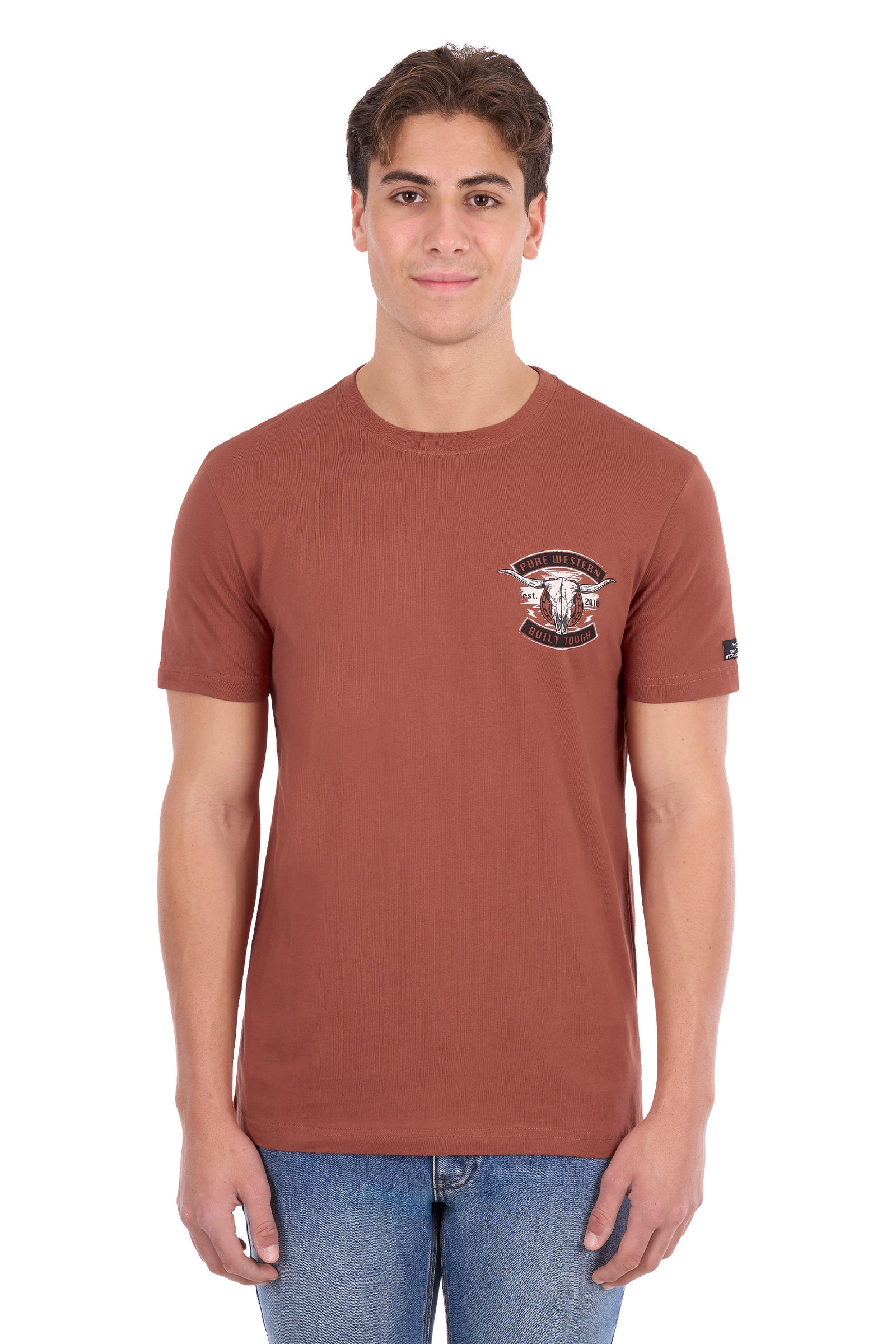 A man wearing a rust-colored short-sleeve t-shirt with a small chest graphic and blue jeans, standing against a plain white background.