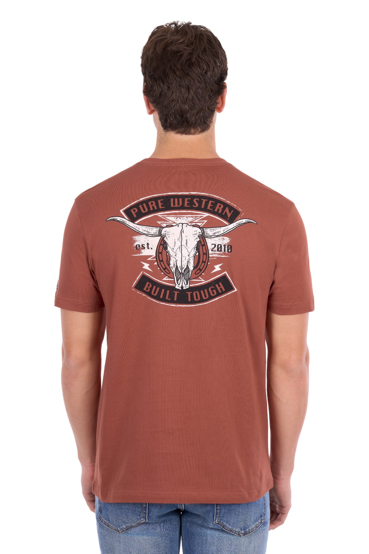 A man viewed from the back wearing a rust-colored t-shirt with a large graphic on the back featuring a steer skull and the text 'PURE WESTERN BUILT TOUGH'.