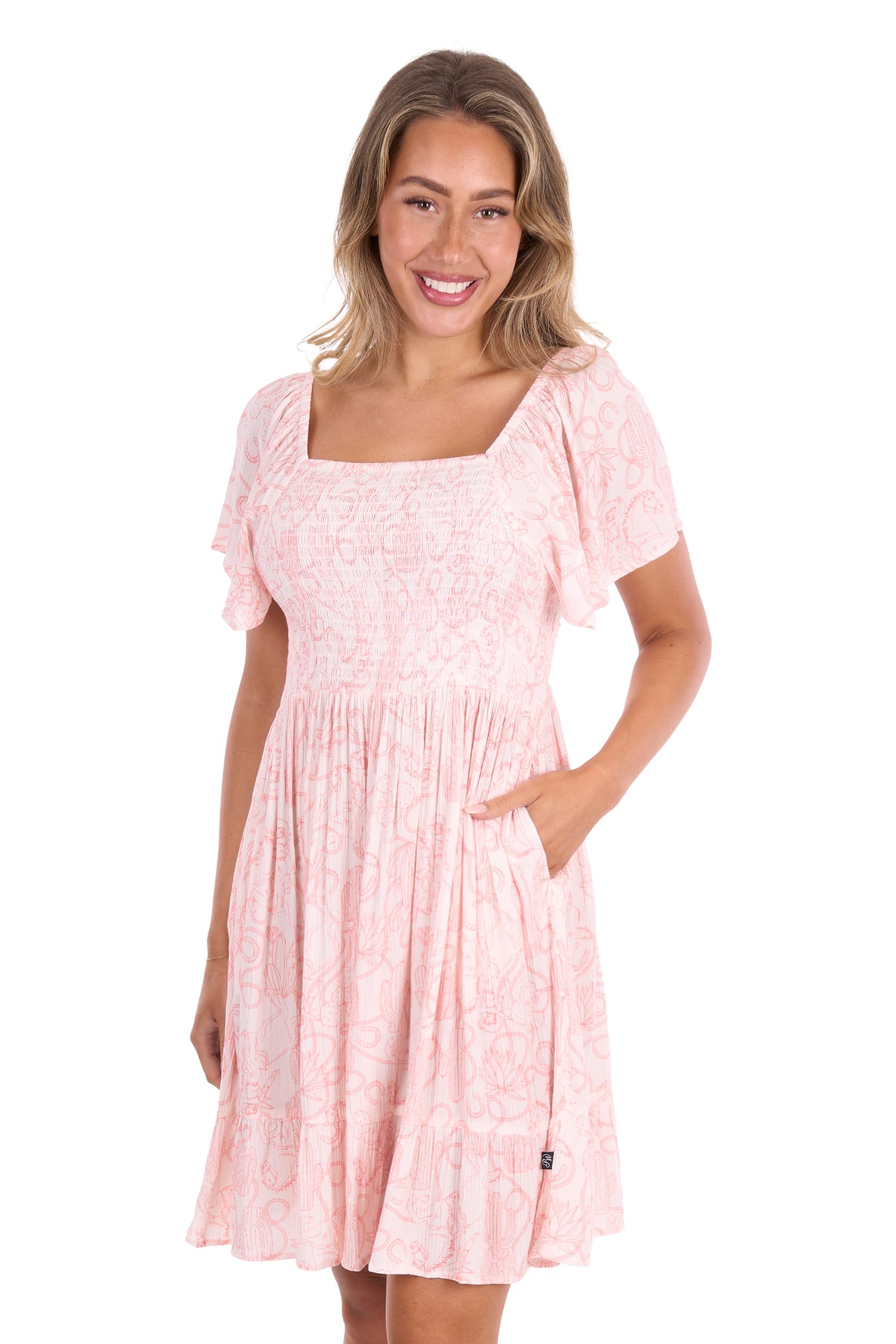 A woman modeling a light pink short-sleeve dress with a tonal floral pattern, square neckline, and side pockets against a plain white background.