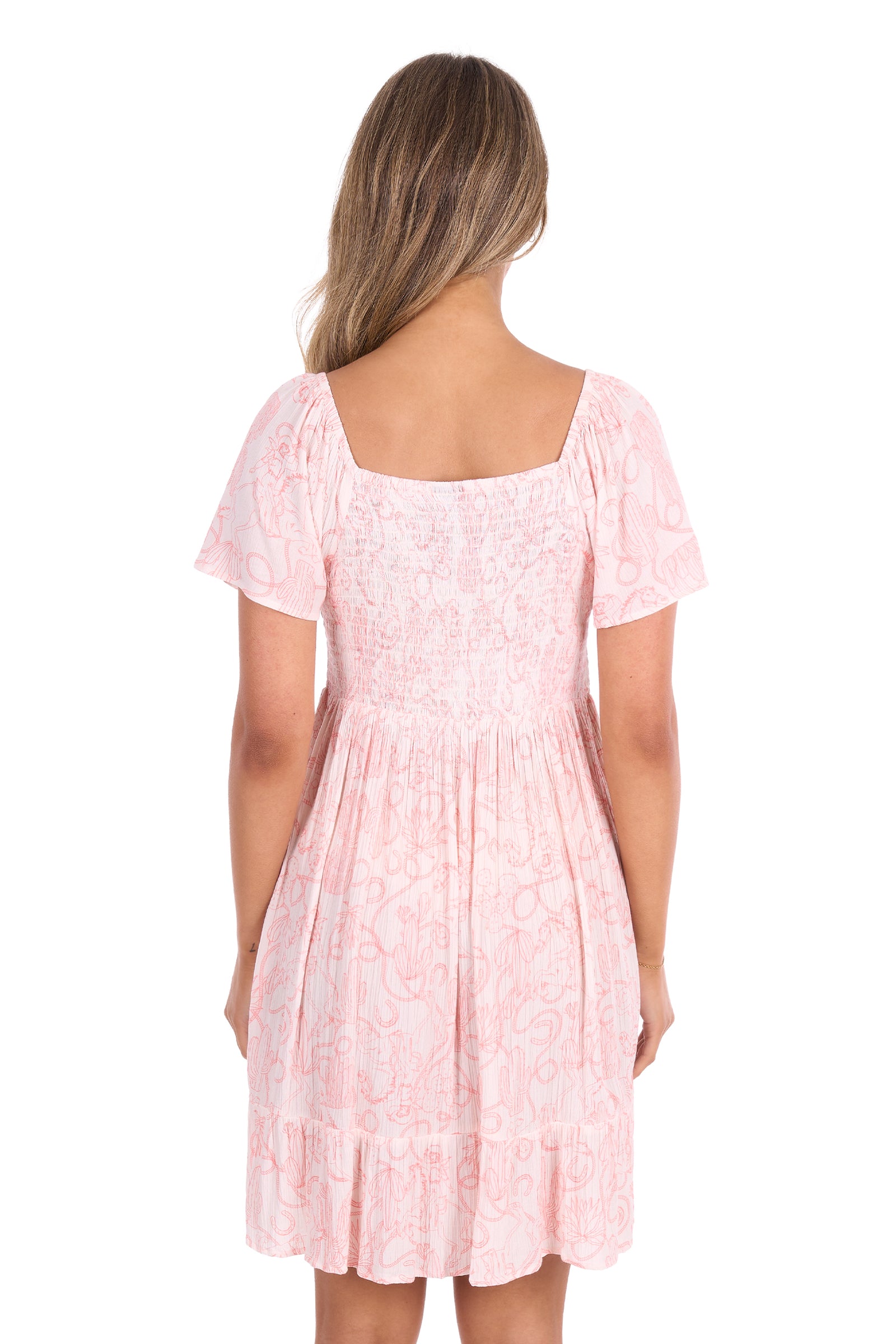A woman viewed from the back wearing a light pink short-sleeve dress with a smocked bodice and ruffled hem, set against a plain white background.