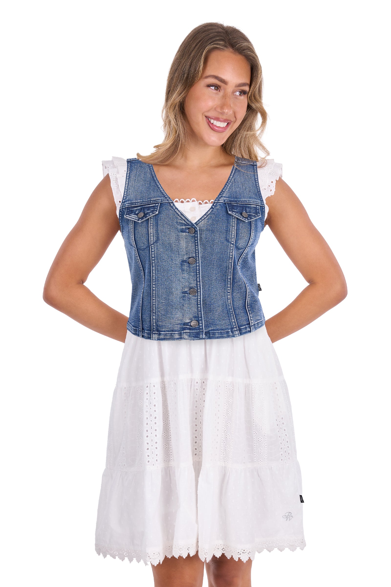 A woman modeling a sleeveless blue denim vest with ruffle shoulders over a white eyelet dress, photographed against a plain white background.