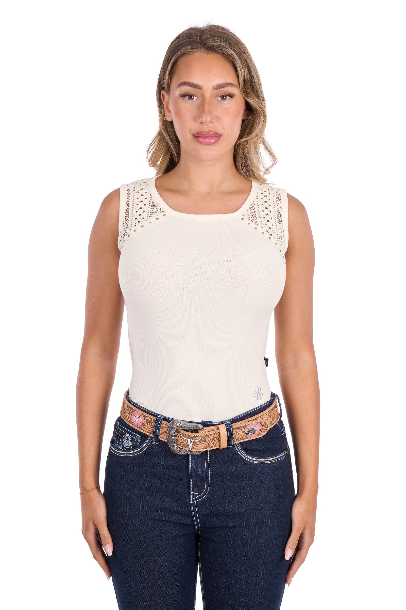 A woman modeling a sleeveless cream-colored top with delicate lace detailing on the shoulders, paired with dark blue jeans and a western-style belt, against a plain white background.