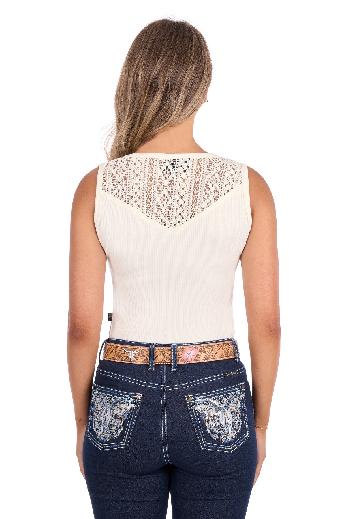 Rear view of a woman wearing a sleeveless cream top with a lace yoke and dark blue jeans with embroidered back pockets, on a white background.