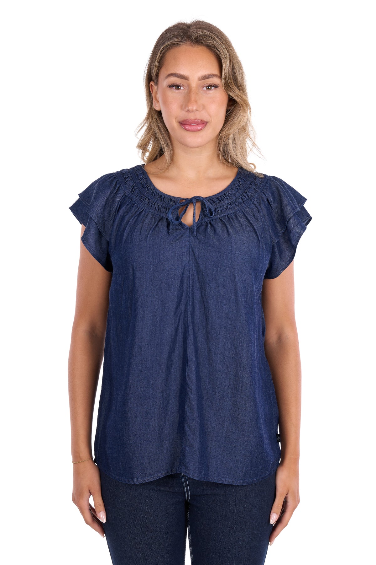 A woman modeling a dark blue chambray short-sleeve blouse with a keyhole cutout and ruffled details, paired with dark blue jeans against a plain white background.