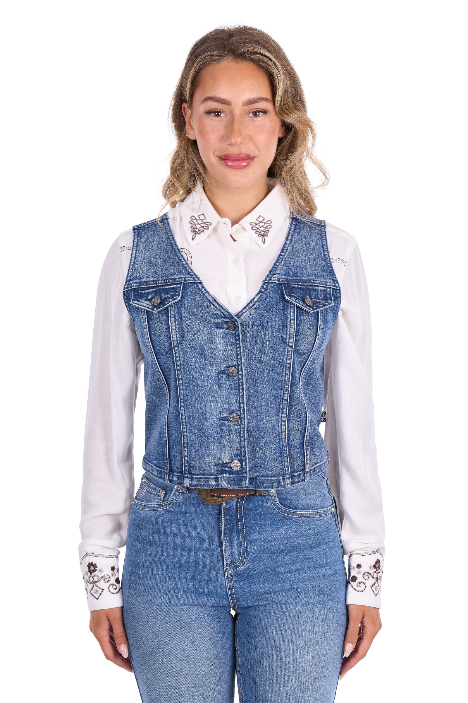 A woman modeling a blue denim vest over a white embroidered collared shirt and blue jeans, photographed against a plain white studio background.