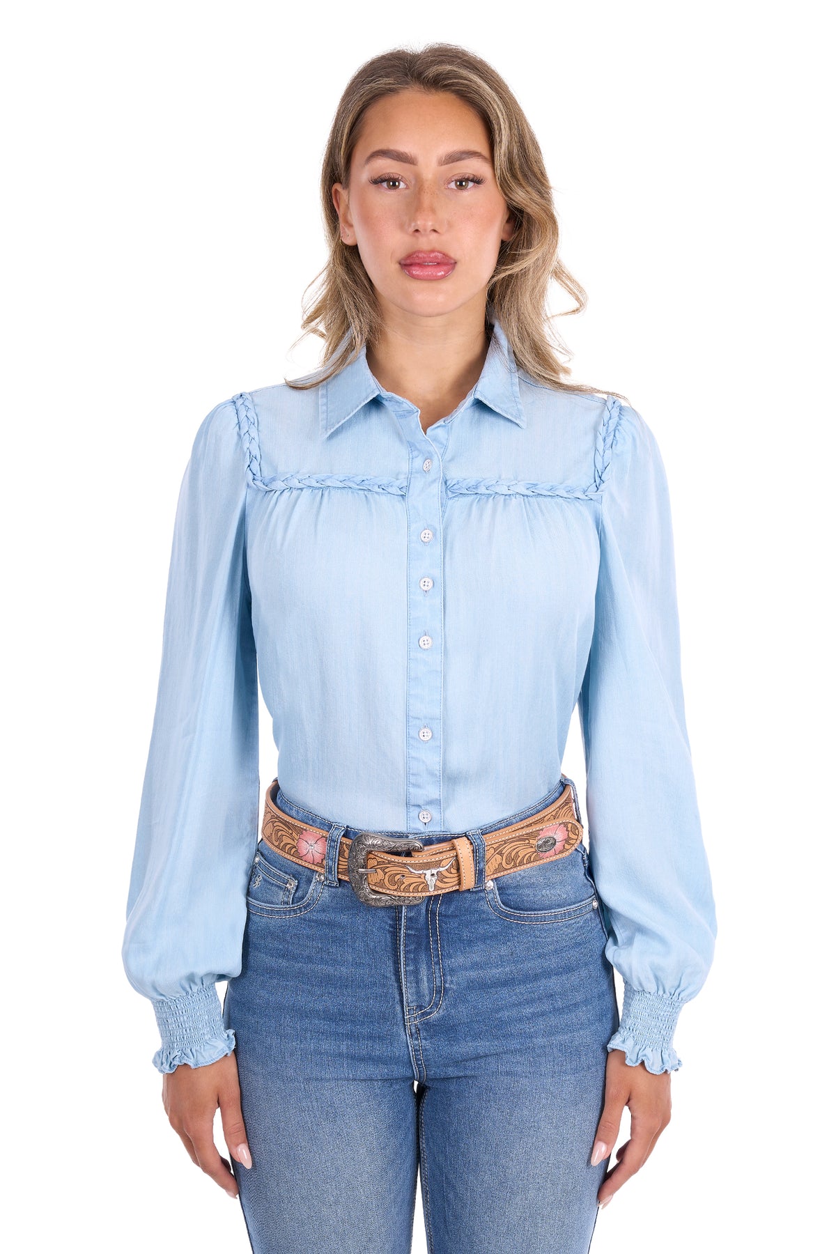 A woman modeling a light blue long-sleeve western-style button-up shirt with ruffle trim, paired with blue jeans and a patterned belt, against a plain white background.