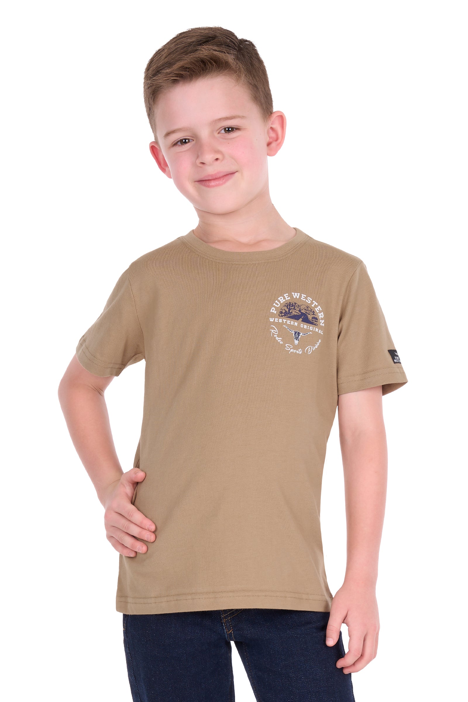 A young boy modeling a tan crewneck t-shirt with a circular chest graphic and a small patch on the sleeve, paired with dark blue jeans against a plain white background.