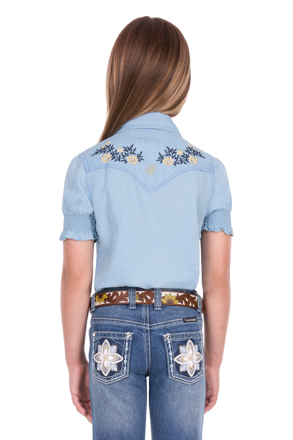 A model shown from the back wearing a light blue denim western shirt with embroidered floral details on the shoulders and blue jeans with star embroidery on the back pockets.