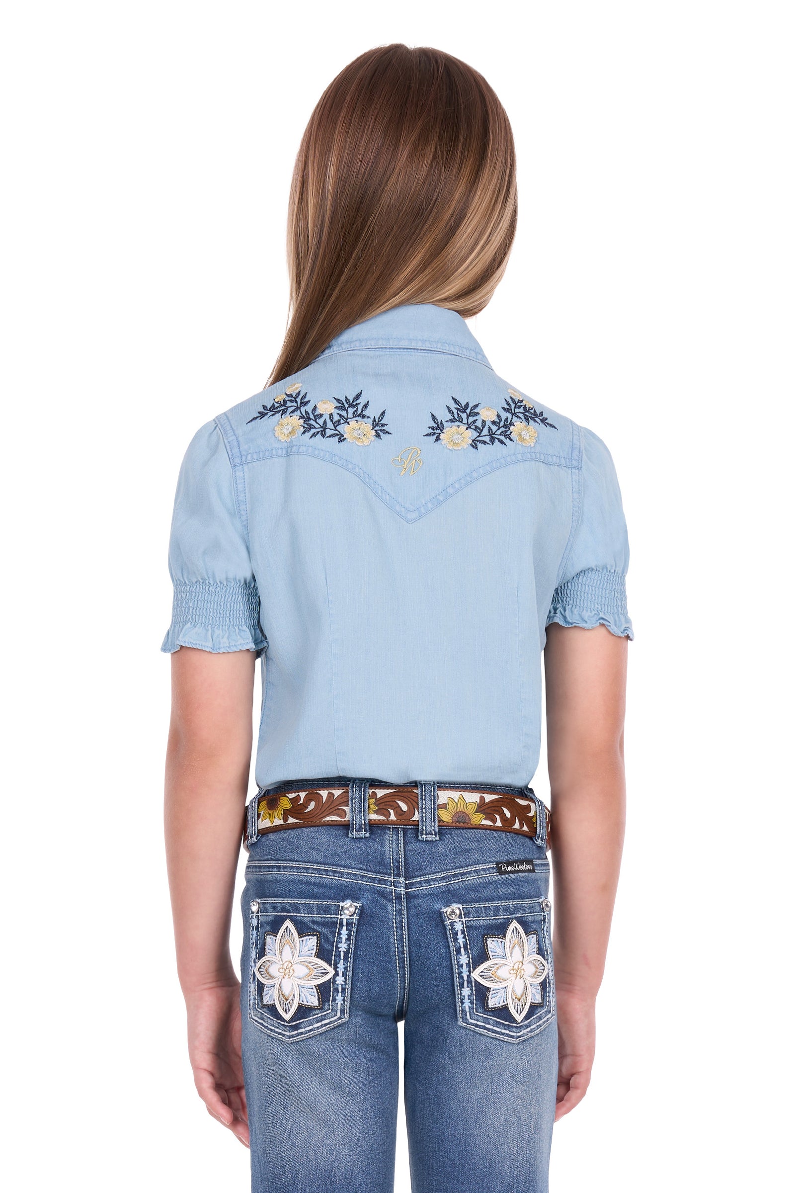 A model shown from the back wearing a light blue denim western shirt with embroidered floral details on the shoulders and blue jeans with star embroidery on the back pockets.
