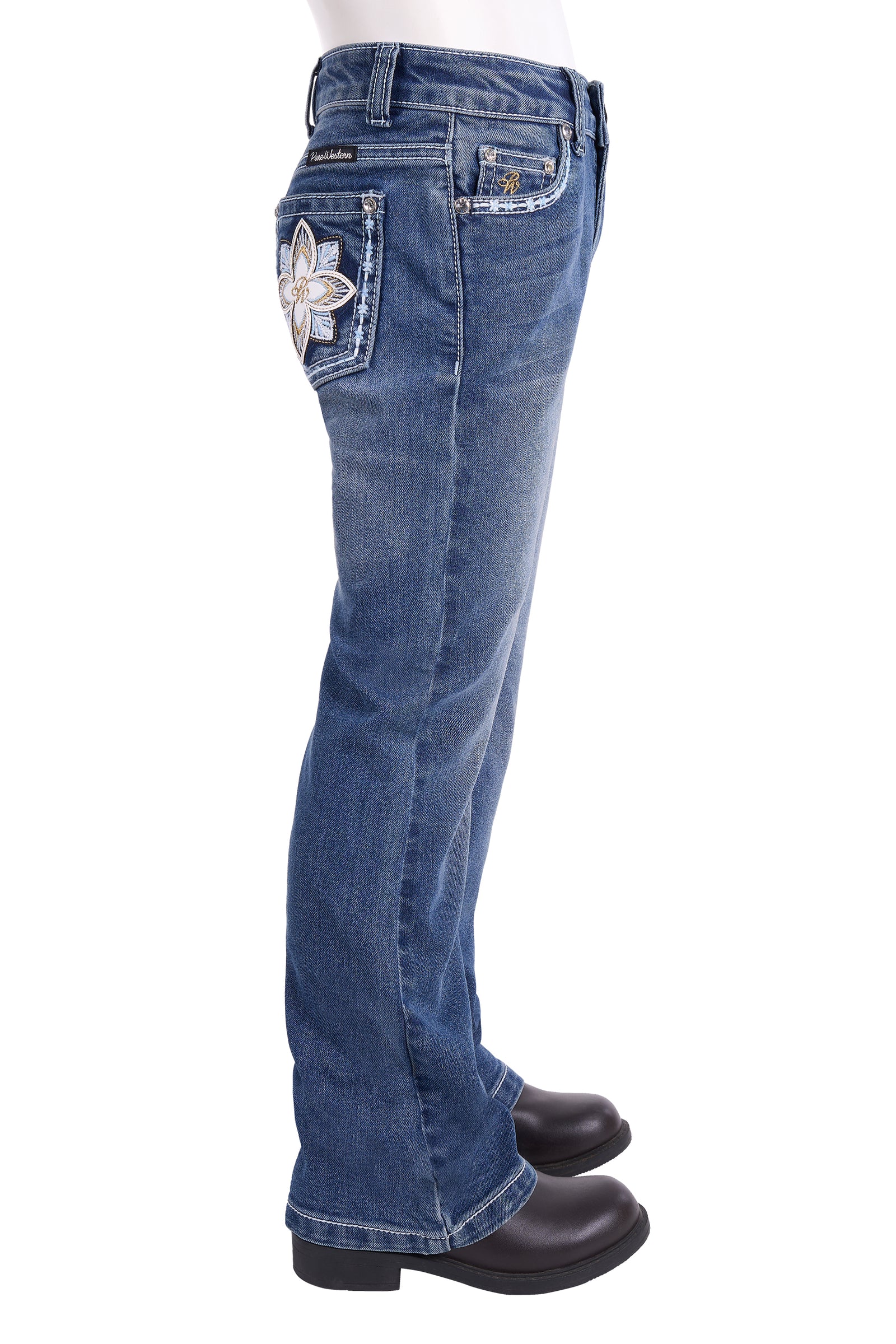 Side view of a pair of blue denim jeans with a large white embroidered flower patch on the back pocket, shown on a white background with black boots.