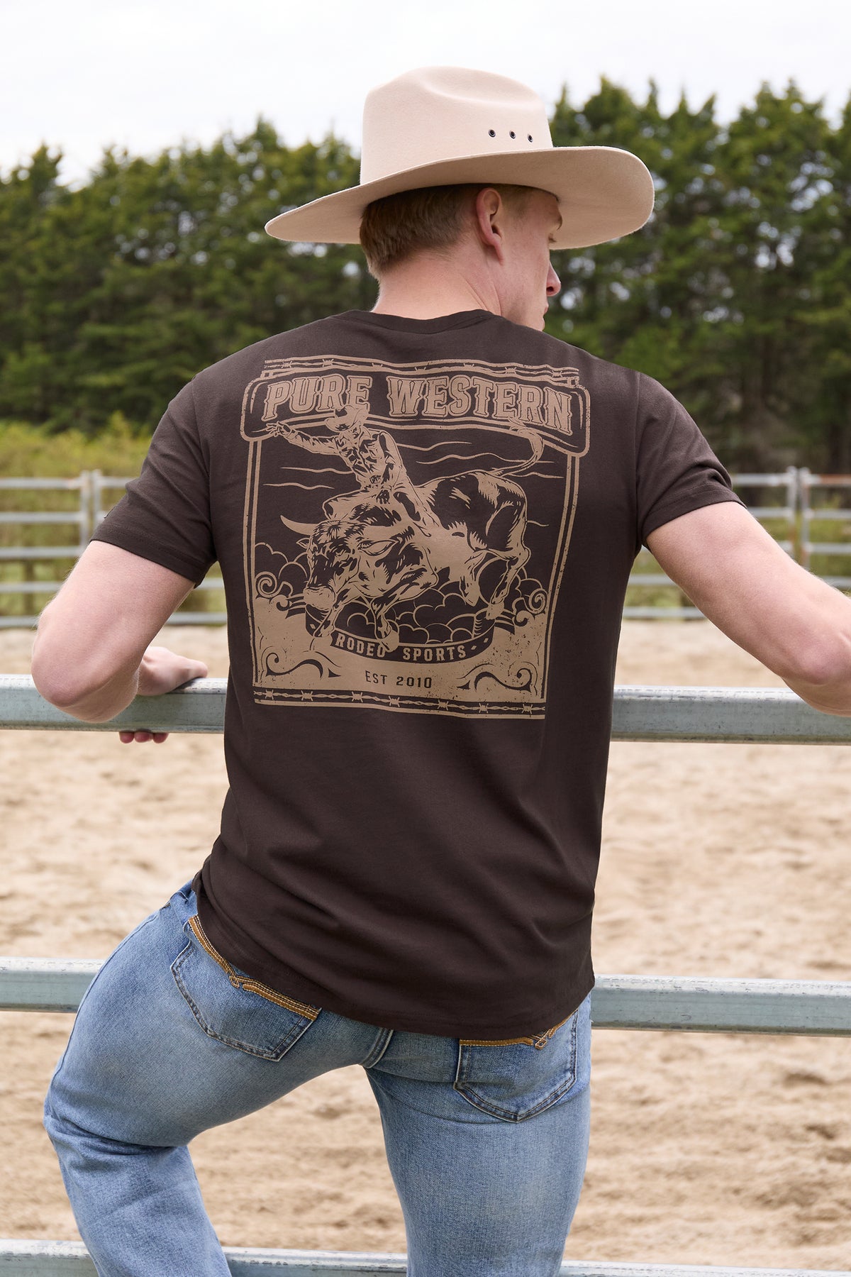 Person wearing a brown 'Pure Western' t-shirt with a graphic design, standing in an outdoor setting.