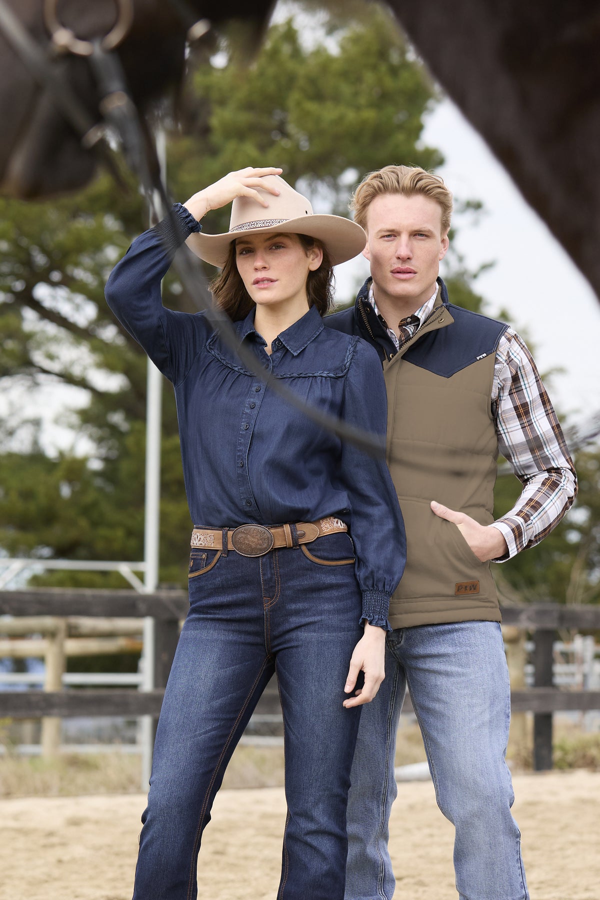 Two people in outdoor attire with a horse in the background