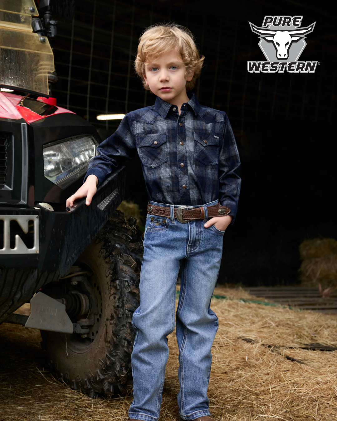 Young boy in a plaid shirt and jeans standing next to a truck with 'Pure Western' branding.