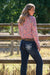 Pure Western Women's Lyn Relaxed Rider Jean. Woman wearing a pink floral shirt and dark jeans standing near a wooden fence with greenery in the background.