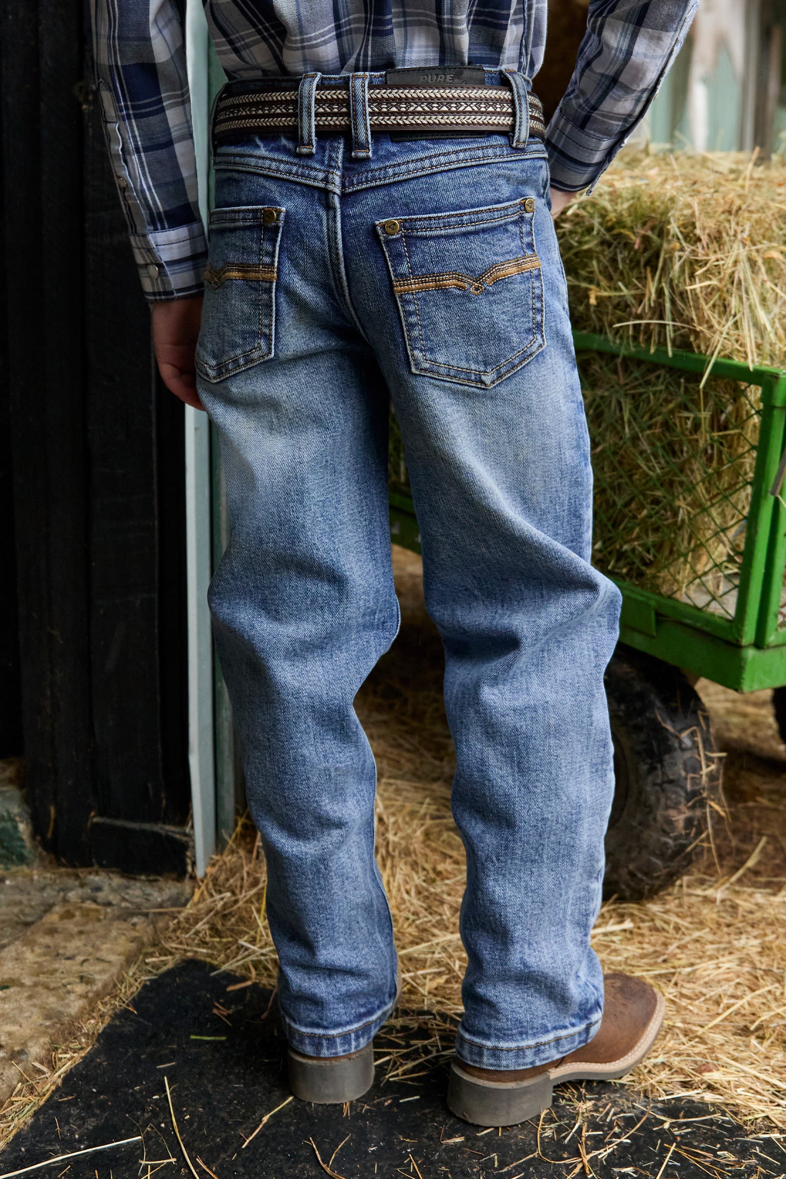 Person wearing blue jeans standing in a barn with hay and a green cart.