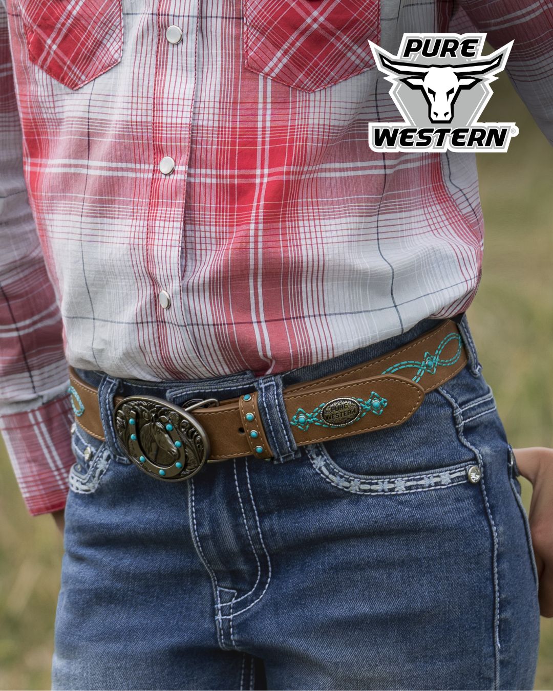 A close-up of a person wearing a brown western belt with turquoise accents and a large engraved buckle, paired with blue jeans and a red-and-white plaid shirt. The Pure Western logo appears in the top right corner.