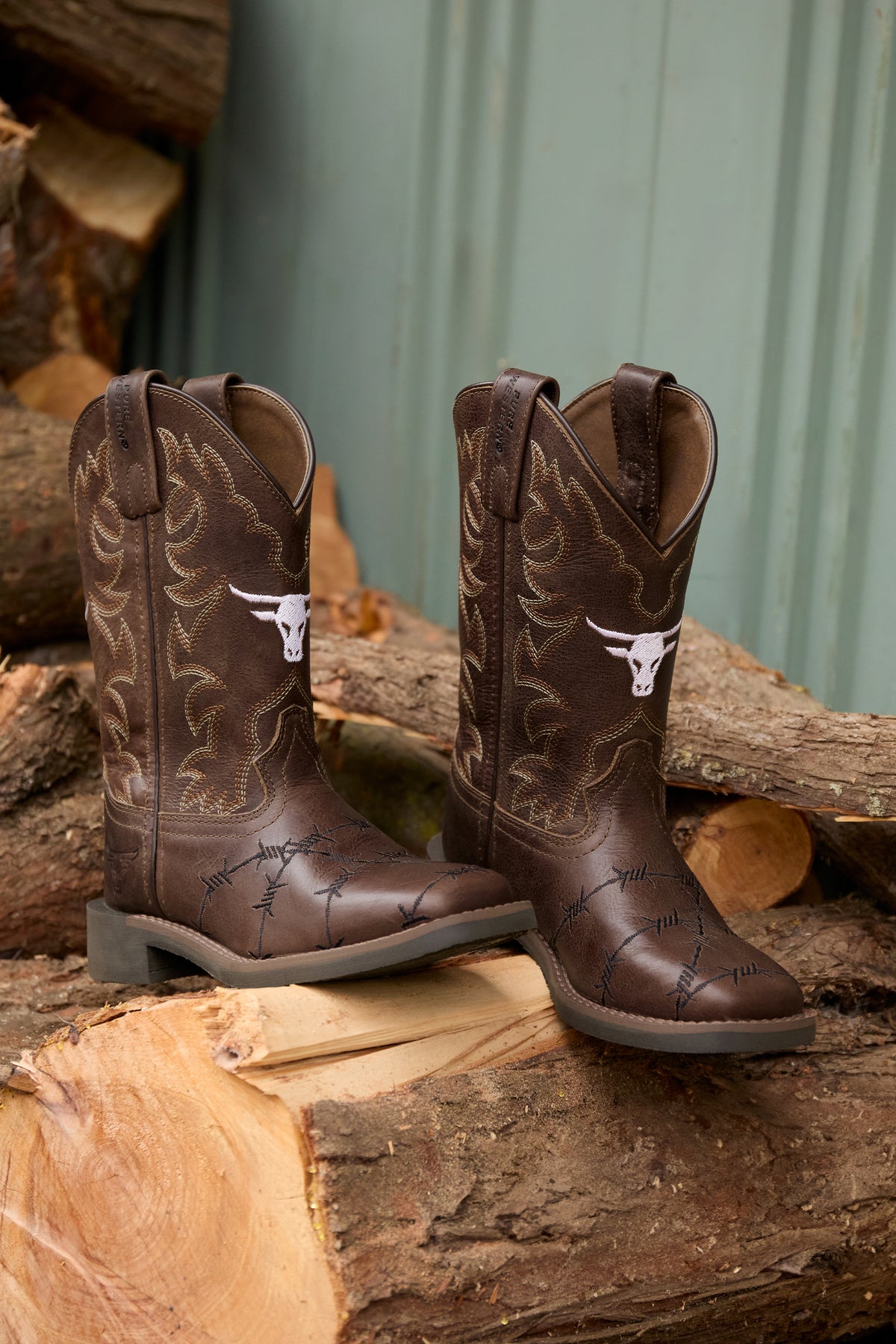 Pair of brown cowboy boots with white bull logo on a wooden surface