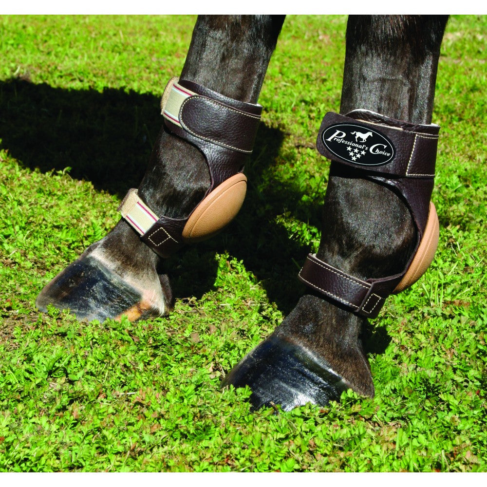 A pair of brown leather skid boots with straps and a brand logo on the top strap, fitted on a horse's front legs.