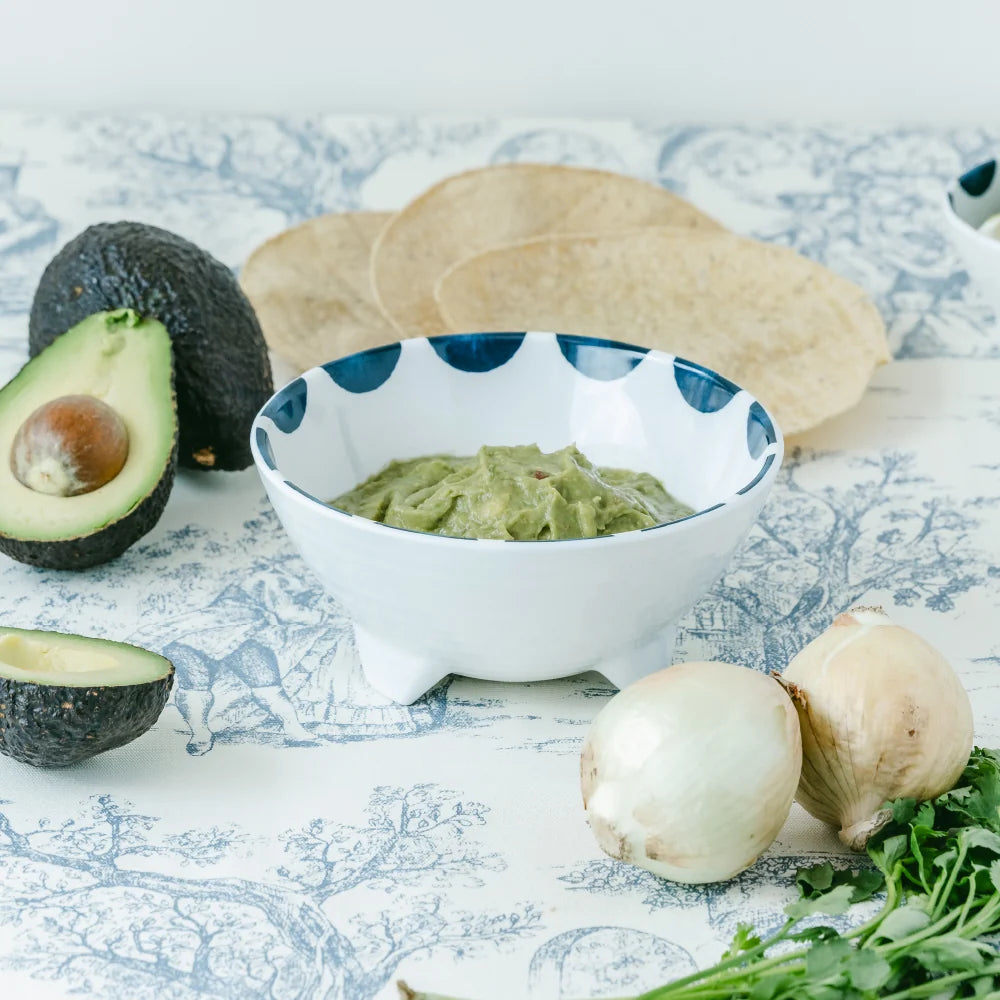 Bowl of guacamole with avocados, tortillas, and mushrooms on a patterned tablecloth