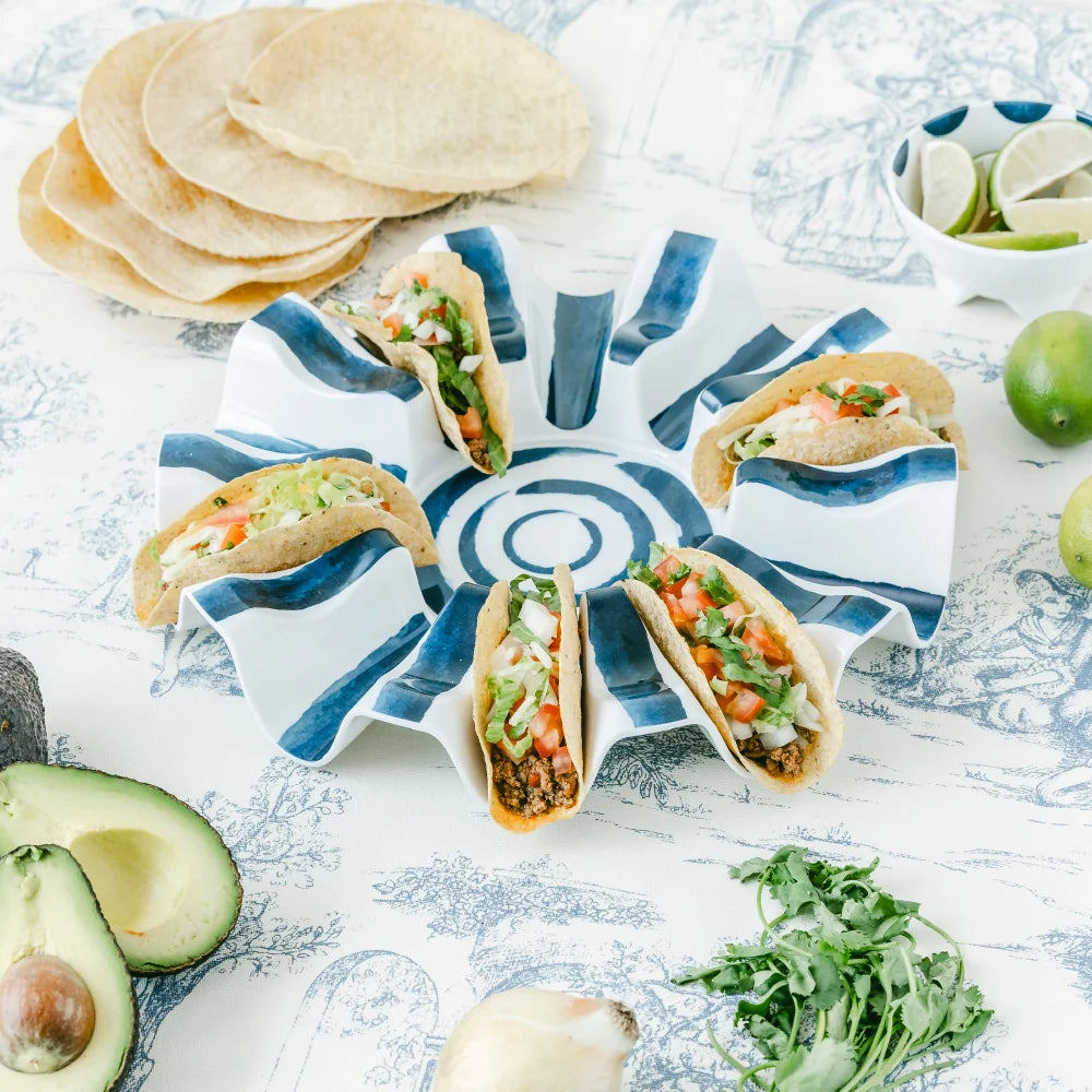 Tacos on a decorative plate with tortillas, avocados, and limes on a textured surface.