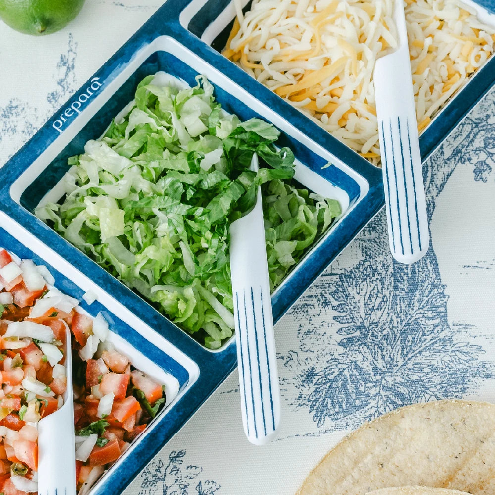 Prepared food items including lettuce, cheese, and tomatoes in blue containers on a patterned tablecloth.