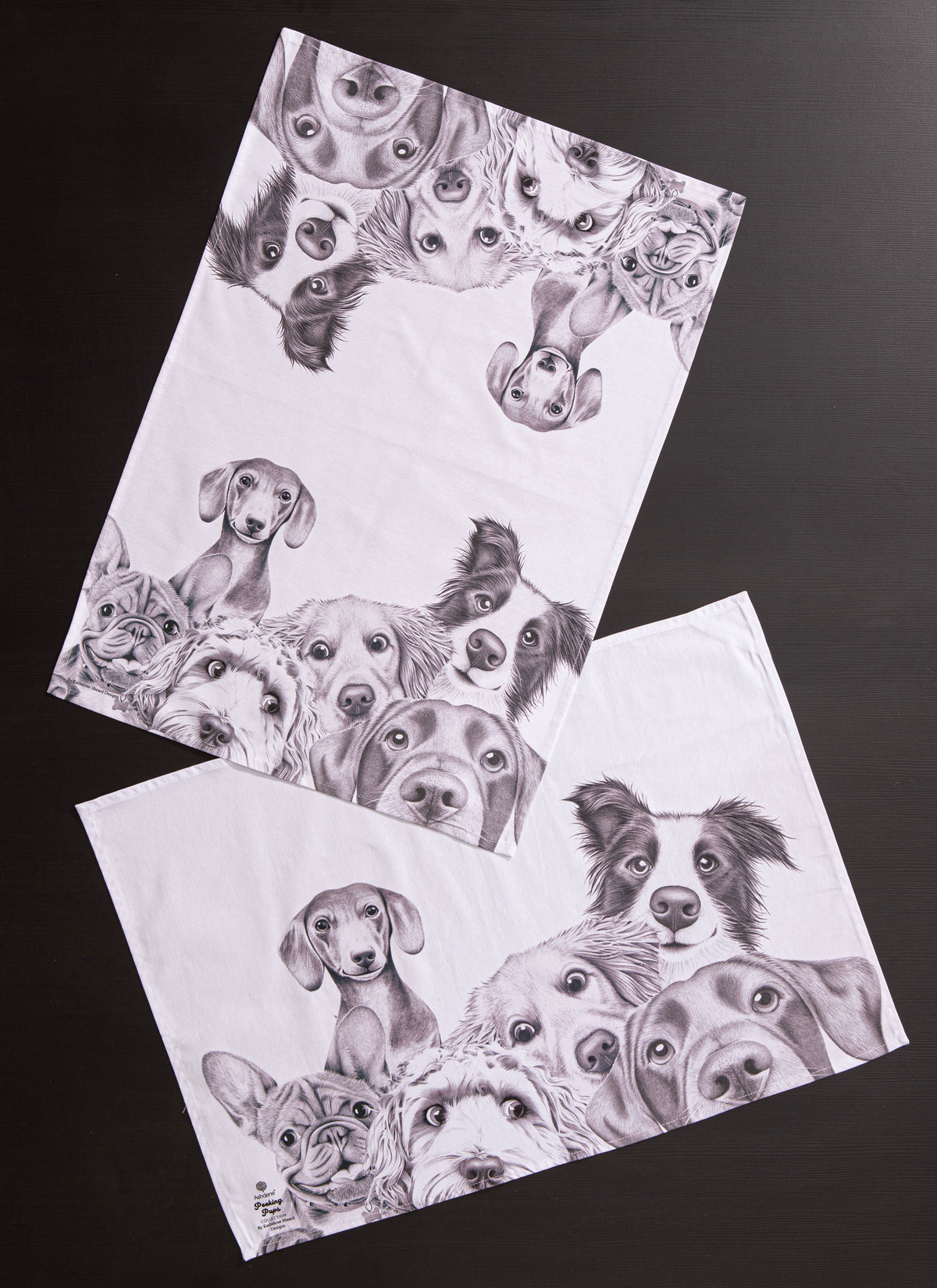 Two white towels with black and white illustrations of dogs on a dark background