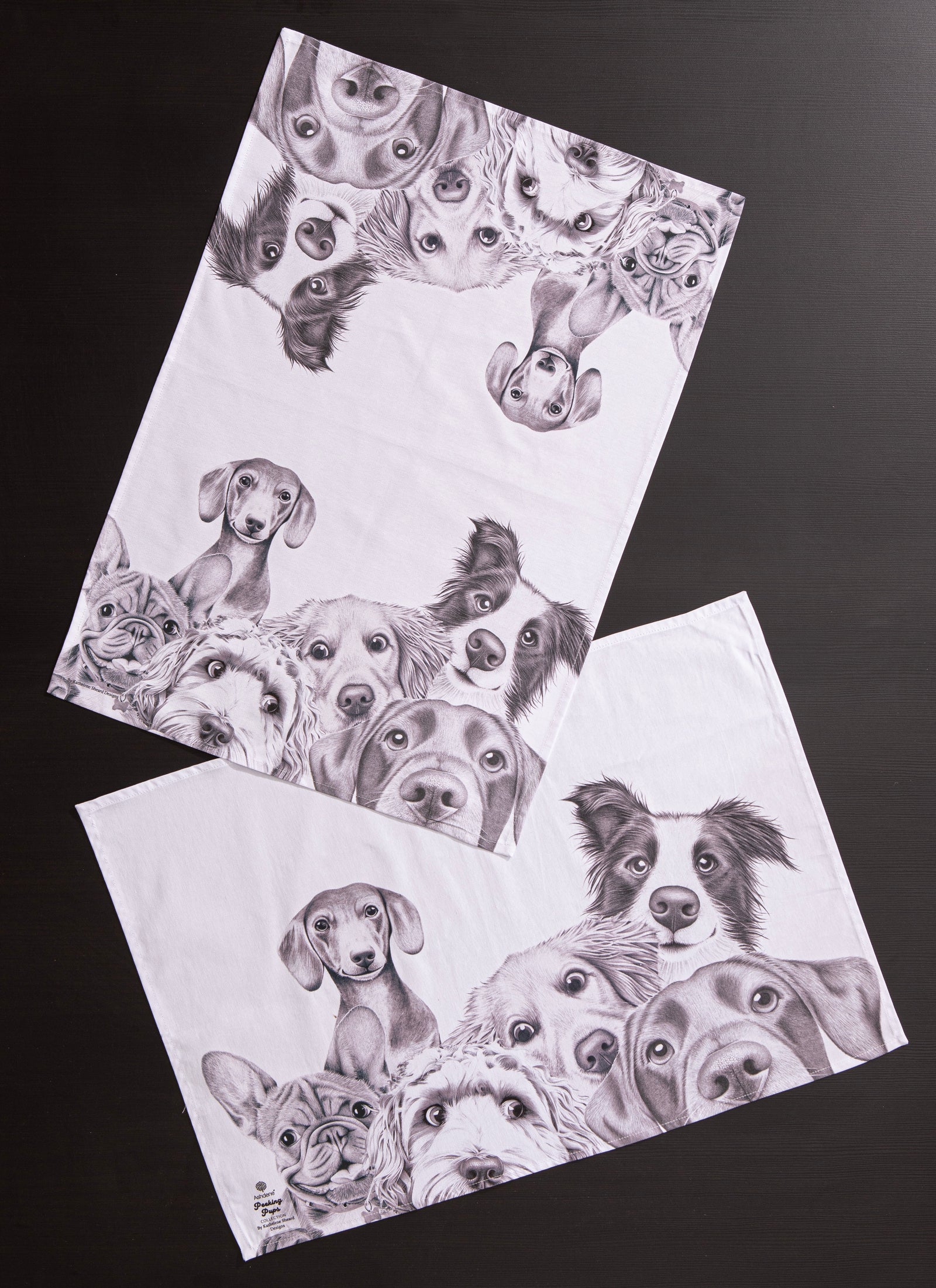 Two white towels with black and white illustrations of dogs on a dark background