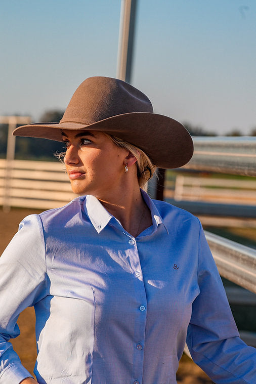 Reba Women's Blue Bird Oxford Gal L/S Shirt. Person wearing a brown cowboy hat and blue shirt outdoors