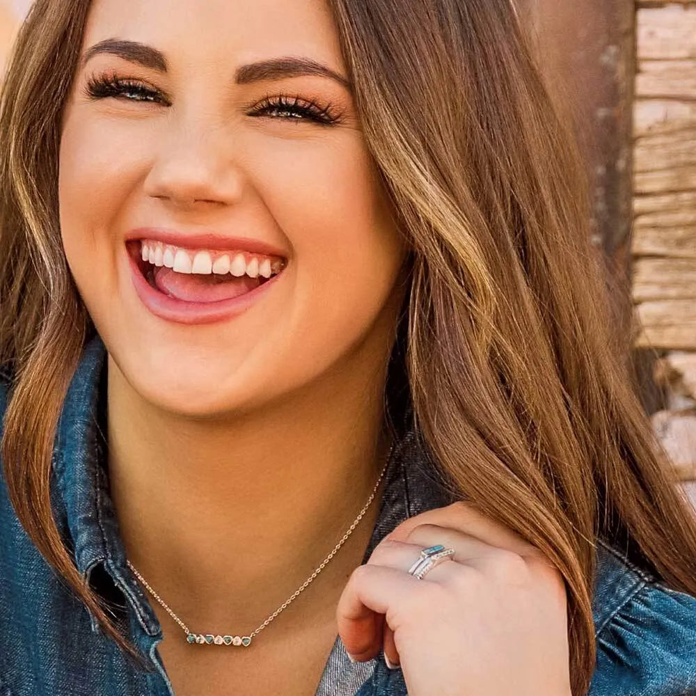 Close-up of a woman with a bright smile, wearing a necklace and ring.