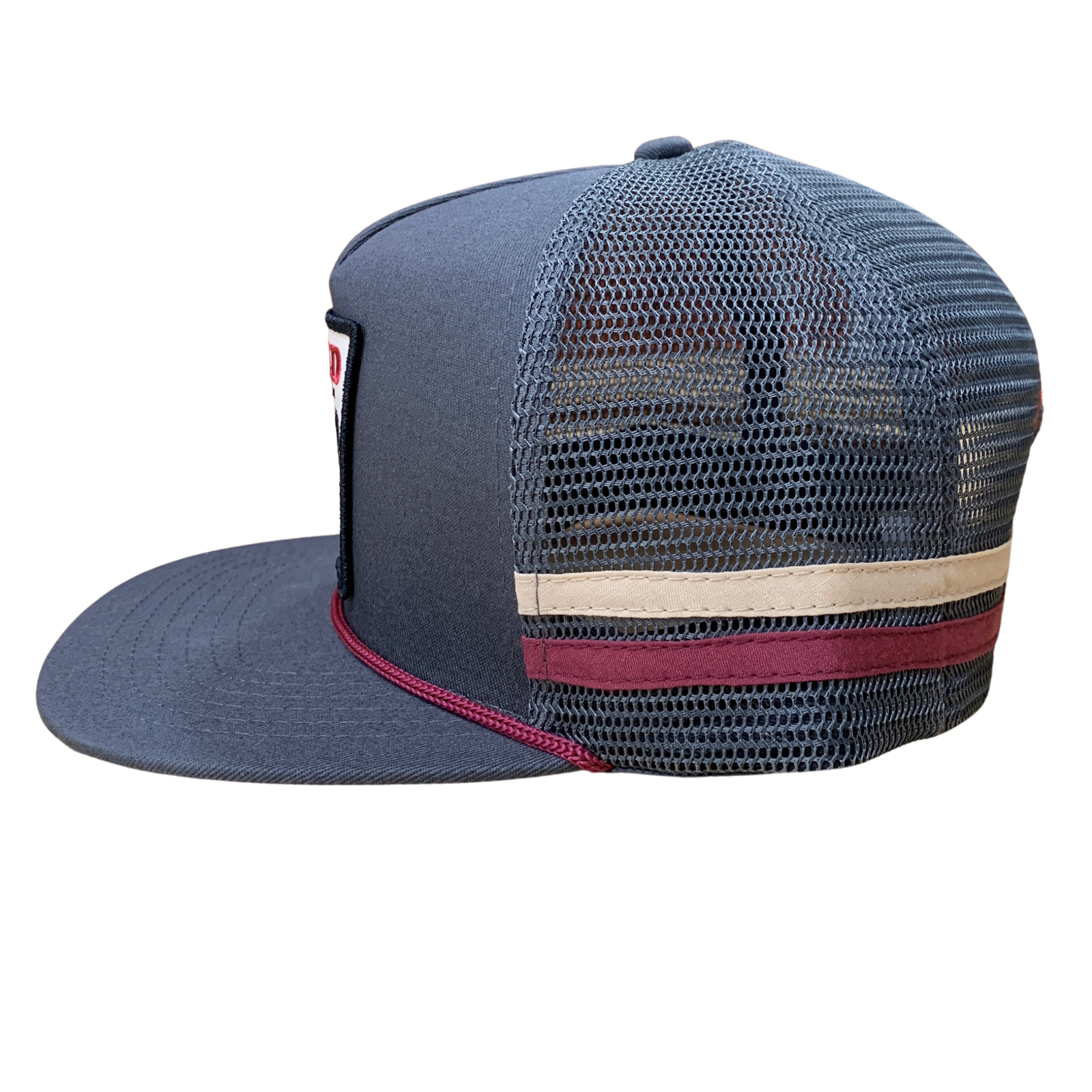 A dark gray trucker cap with a flat brim, featuring a beige horizontal stripe and a burgundy stripe on the back mesh panels, with a small red and white logo patch on the side.