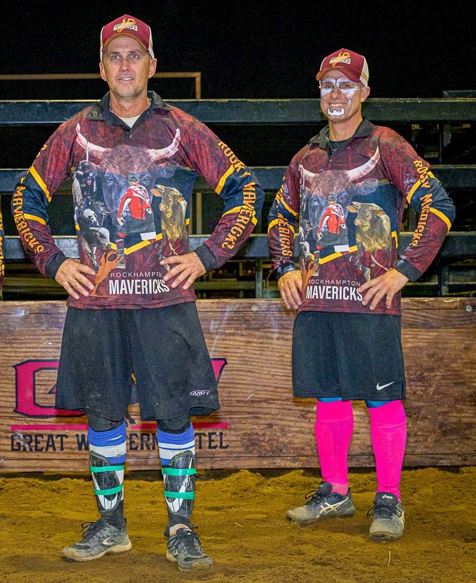 Rocky Mavericks Men's Bull Rider Jersey. Two men wearing matching long-sleeve bull rider jerseys with 'Mavericks' and a bull graphic on the front, standing on a dirt surface with a tent in the background.