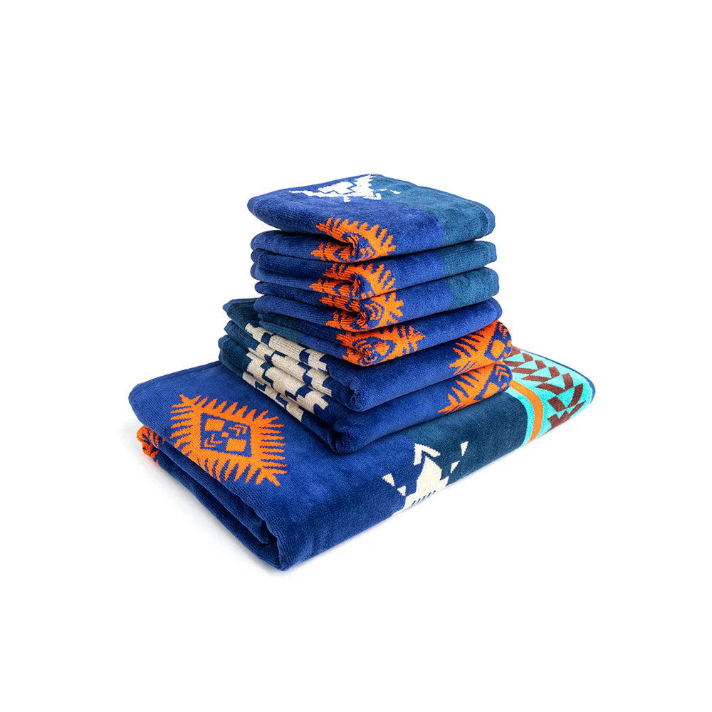 Tribal Rain Towel Set. A set of folded towels in blue, orange, turquoise, and brown with a geometric tribal pattern, stacked on top of each other.