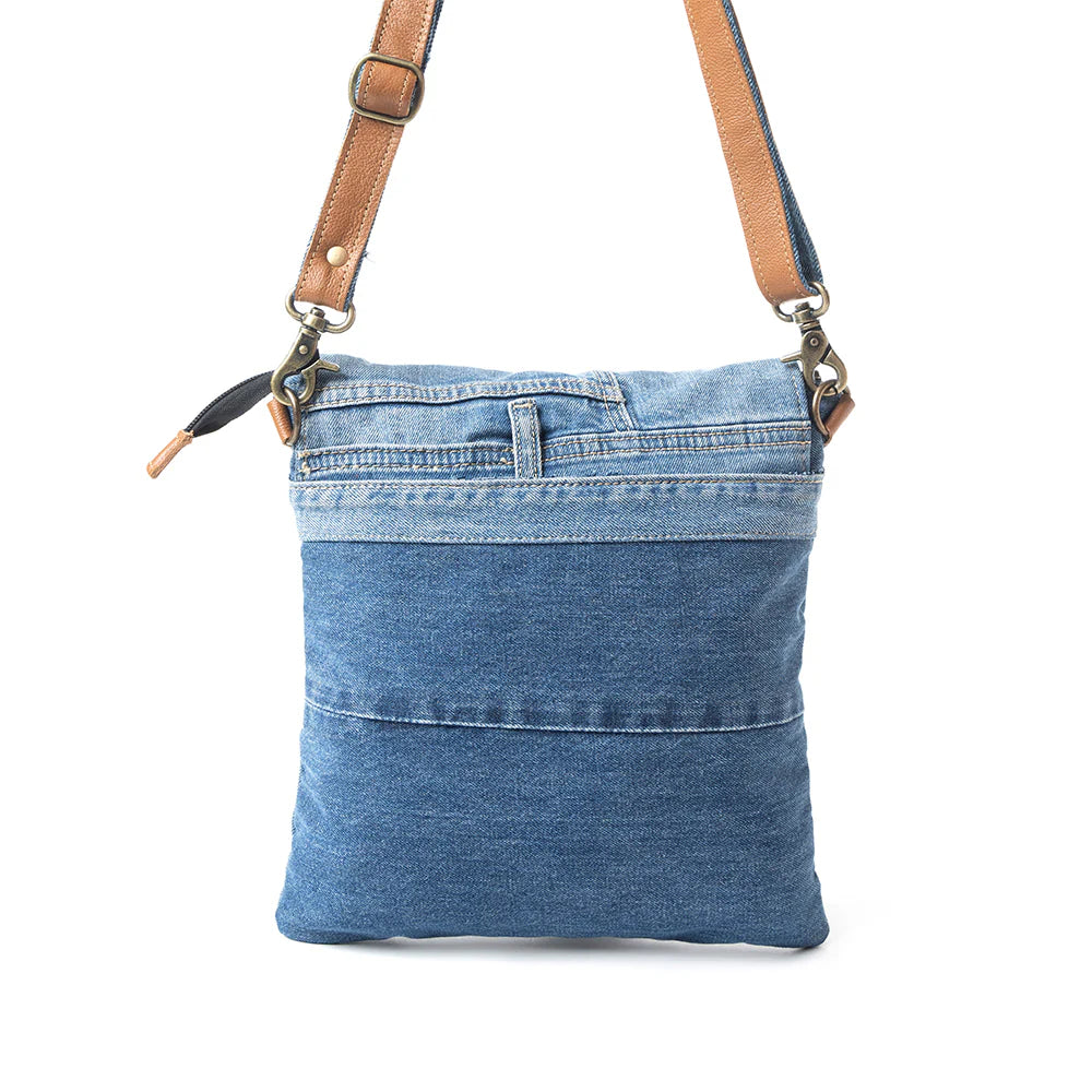 Blue denim crossbody bag with brown leather straps on a white background